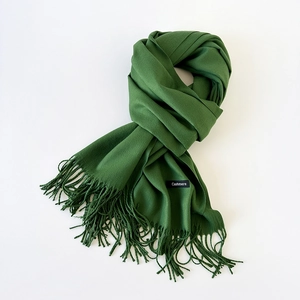 Detailed macro view of dark green scarf showing fringe tassels and cashmere label
