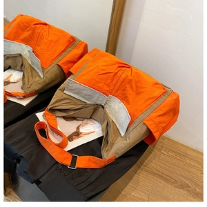 Detail of color-block messenger bag with orange and khaki panels and adjustable metal buckle strap
