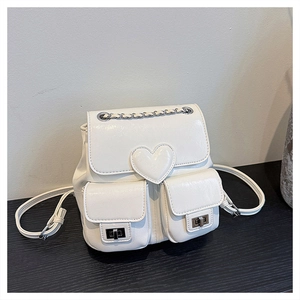 Detail of white mini backpack featuring heart-shaped flap and silver chain handle straps