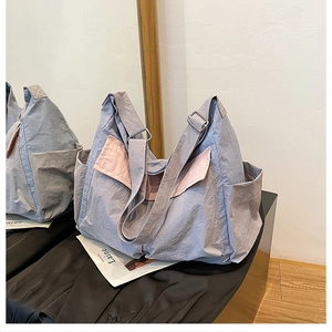 Detail view of a large blue and pink canvas messenger bag on a black bench with magazine