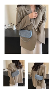 Detail of light blue denim handbag with silver studs and chain strap shown on a model