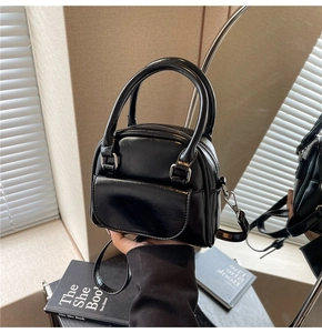Polished black Boston style handbag with top handles and slender shoulder strap detail