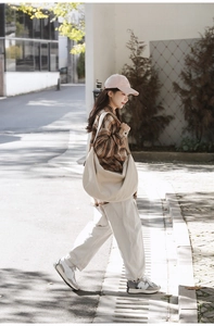 Candid outdoor shot of a woman styling a large beige nylon shoulder bag in a street setting