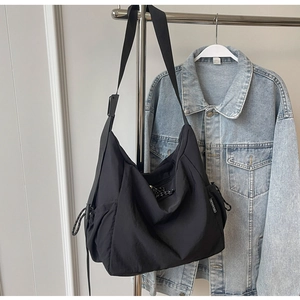 Detail of adjustable side drawstring and brand tag on black nylon large shoulder bag