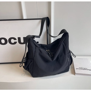 Detail of minimalist black nylon crossbody bag with wide strap and side drawstring pocket