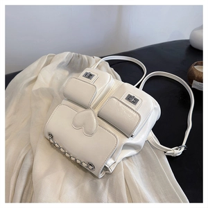 Detail view of white leather backpack with heart patch, metal locks and silver chains