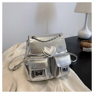Detail of silver metallic backpack featuring heart patch, chain strap, and turn-lock pockets