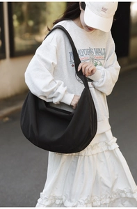 Detailed side view of a large black nylon tote bag worn by a model on a street