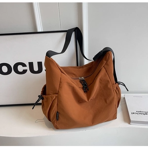 Detail of a brown nylon crossbody bag with adjustable strap and drawstring side pocket