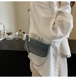 Detail of blue denim crossbody bag with silver studs and chain strap on a white shirt