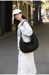 Outdoor street view of a black crescent nylon shoulder bag with high capacity and minimalist design