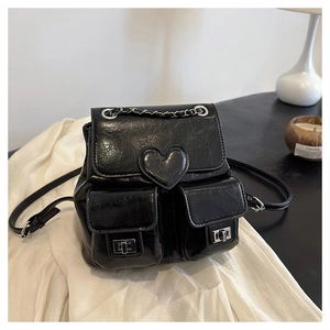 Detail of black glossy leather backpack featuring heart decor and metal chain handles
