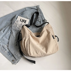 Detail of beige canvas crossbody bag featuring adjustable black strap and drawstring side pocket