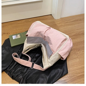 Detail view of large pink and beige nylon crossbody bag with side pocket and gray straps