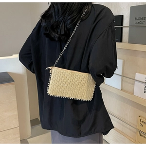 Detail showing beige woven straw shoulder bag with silver studs and thin metal chain strap