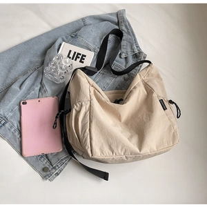 Detail of beige canvas crossbody bag featuring adjustable strap and side drawstring accent