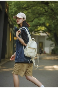 Dettaglio ravvicinato di un mini zaino in nylon color crema con coulisse e tasche con zip