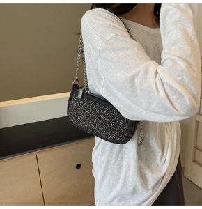 Detail of black rhinestone shoulder bag with silver chain strap worn by a model