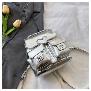 Detail of silver metallic bucket backpack with heart patch and chain handle on fabric