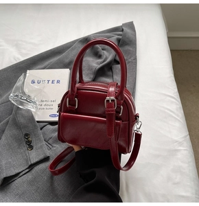 Burgundy mini Boston bag with round handles and adjustable strap on a minimalist background