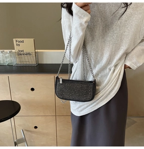 Detail of a chic black rhinestone evening bag with silver chain strap on a model