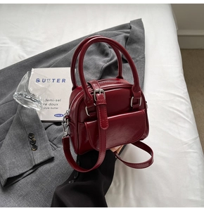 Detailed close-up of dark red glossy patent leather handbag with dual round handles