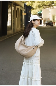 Outdoor shot of a beige nylon crescent bag worn as a shoulder tote by a model