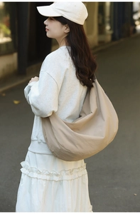 Detailed view of a large beige nylon crescent tote bag worn by a model in outdoor lighting