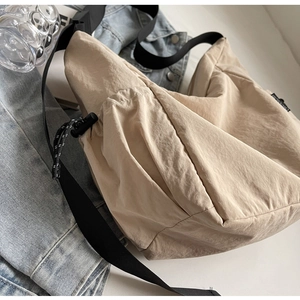 Detail of beige canvas crossbody bag with adjustable black strap and drawstring pocket