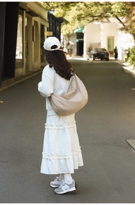 Outdoor shot of a beige crescent nylon tote bag styled with white streetwear fashion
