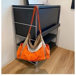 Detail of a large capacity orange canvas crossbody bag with khaki stitching on metal rack