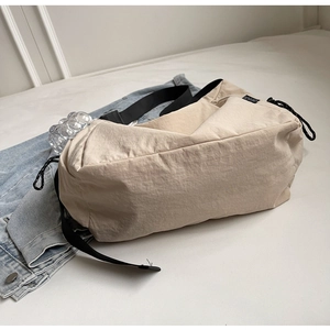Detail of beige nylon crossbody bag featuring black adjustable drawstrings and side brand label