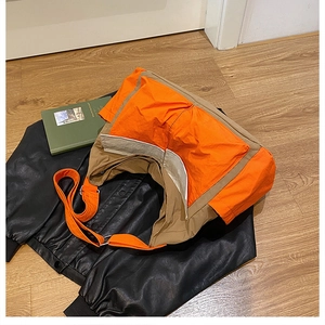 Detail of color-block canvas crossbody bag in orange and khaki on wooden floor