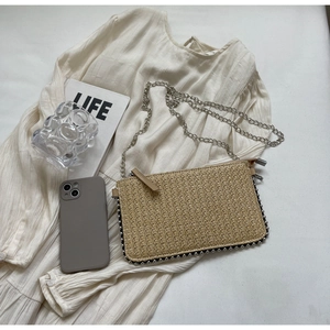 Detailed macro view of woven straw crossbody bag with silver bead trim and metal chain strap