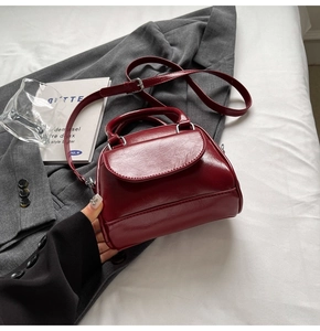 Detail of burgundy glossy pleated leather handbag with silver hardware and top handle