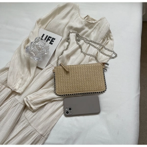 Detail shot of straw woven crossbody phone bag with metal beads on a white bed sheet