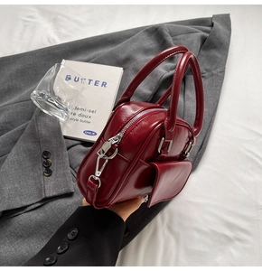 Detail of burgundy glossy Boston bag with silver hardware on a gray blazer backdrop