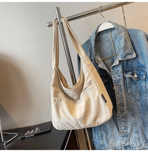 Detail of a large beige canvas shoulder bag hanging with a denim jacket and book