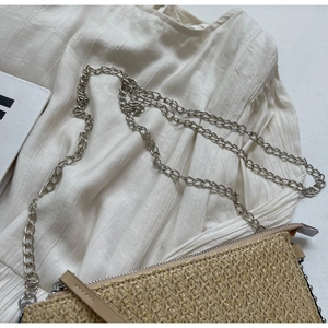 Detail of beige straw crossbody bag with V-shaped weave and silver chain strap