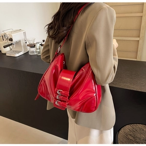 Detailed view of a shiny red patent leather hobo bag with three silver decorative buckles