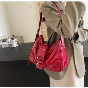 Detail of red patent leather shoulder bag with silver triple buckle straps on a model