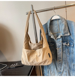 Close-up of beige nylon tote bag with side logo tag hanging on a metal hanger