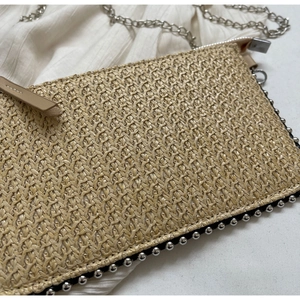 Detail of straw woven envelope bag featuring metal studs and silver chain strap