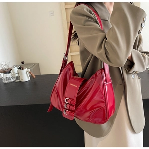 Detail view of bright red patent leather handbag with silver buckles on shoulder