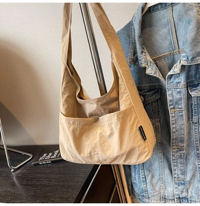 Close-up of beige casual crossbody bag with black woven label hanging on a metal rack
