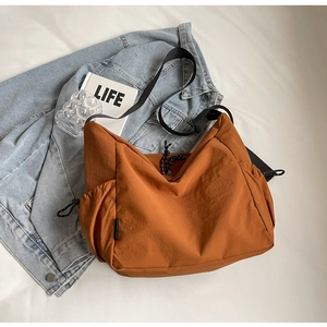 Detailed side view of orange canvas crossbody bag with drawstring pocket and black strap