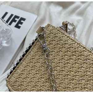 Close-up of woven straw bag with silver stud rivets and a metallic chain strap