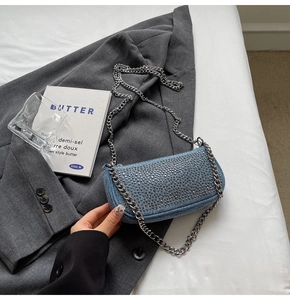 Close-up of light blue denim handbag with silver studs and chain strap on grey blazer