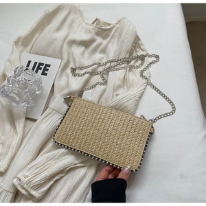 Detail of woven straw crossbody bag with silver bead trim and a fine metal chain strap