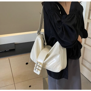Detail view of cream white glossy underarm bag with triple-buckle strap on shoulder